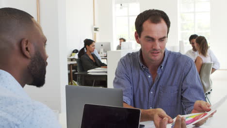 Two-men-discussing-business-documents-in-a-busy-office