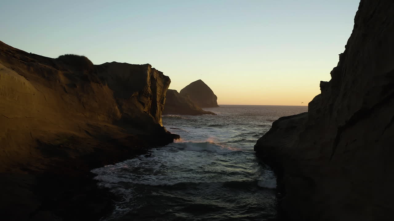 Enseada rochosa de falésia de arenito no Cabo Kiwanda com a rocha Haystack ao pôr do sol.