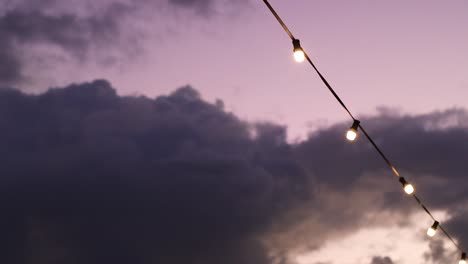 string of glowing outdoor party lights against a beautiful sunset sky at dusk