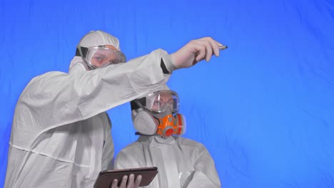 scientist virologist in respirator makes write in an tablet computer with stylus. man and woman wearing protective medical mask. chroma key blue.