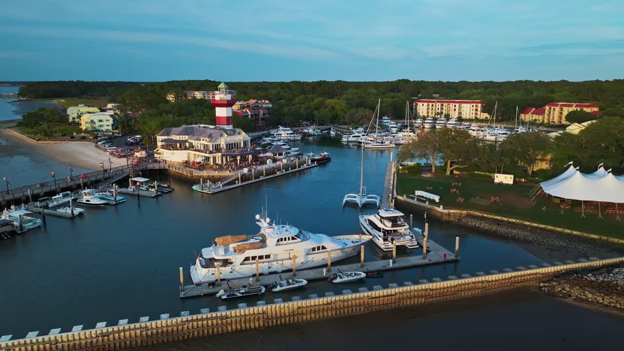 Harbor lighthouse with tourists visible on viewing deck during sunny day, angled approach over yacht, Harbour Town Pier South Carolina USA