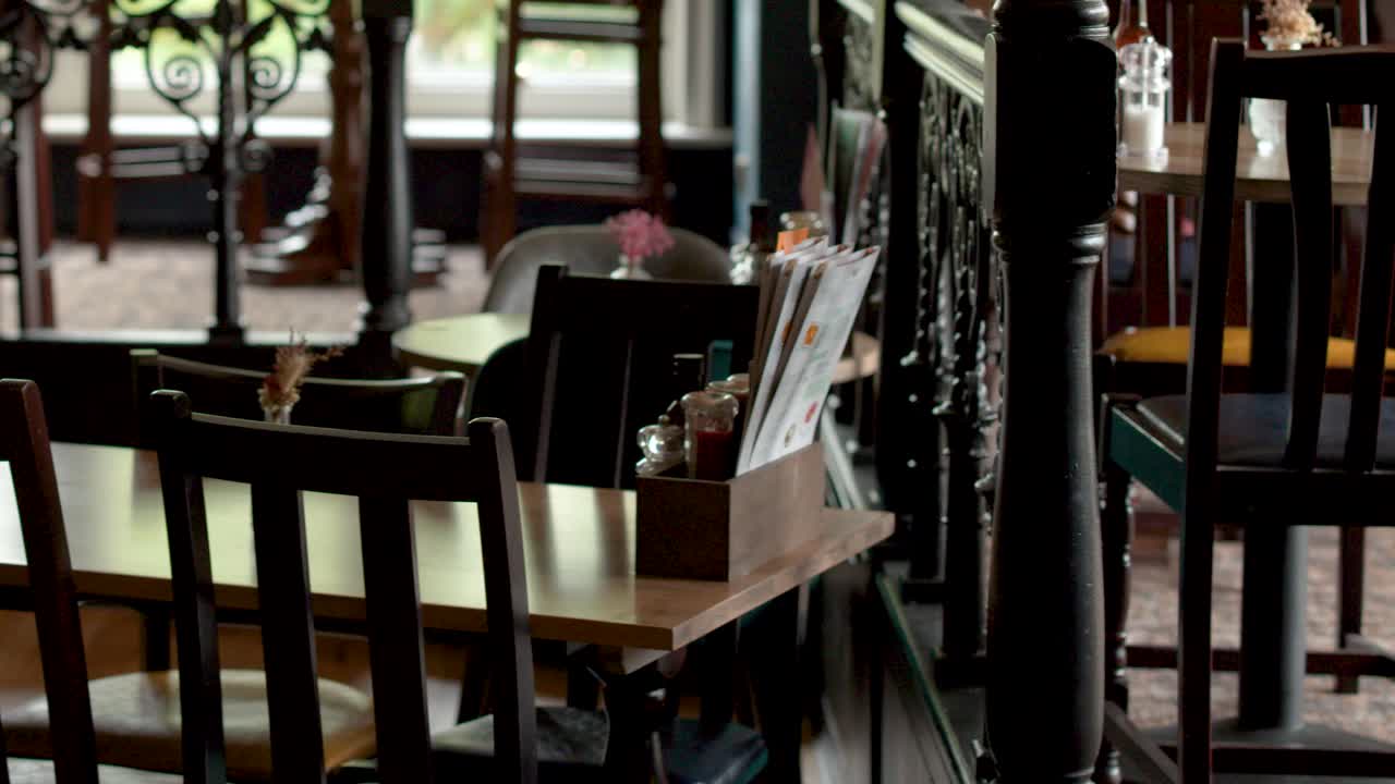 Camera slowly pans through quiet, warmly lit restaurant with wooden tables and chairs, natural daylight