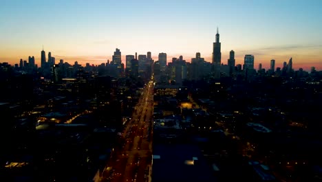 A-captivating-drone-aerial-view-of-a-Chicago-at-dusk,-showcasing-illuminated-skyscrapers-against-the-darkening-sky-The-golden-hues-of-sunset-paint-a-serene-backdrop,-highlighting-architectural-marvels