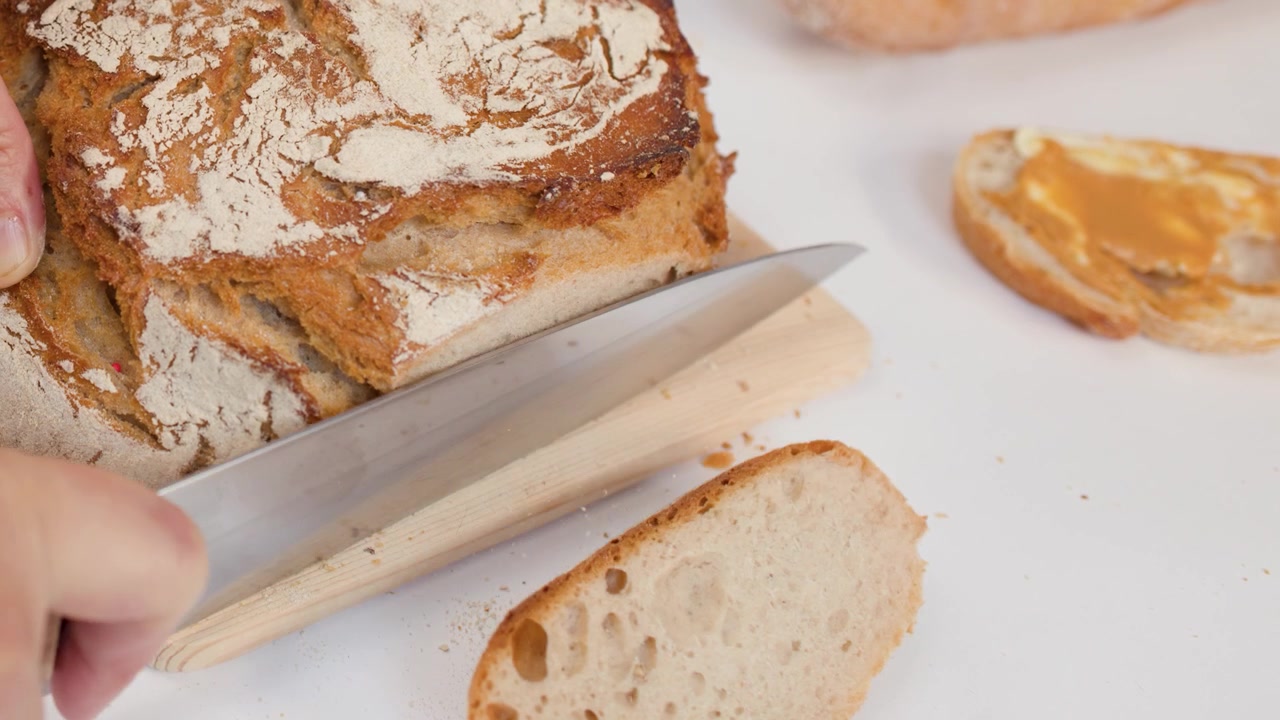 Person Slicing Fresh Crusty Sourdough Bread on Wooden Board
