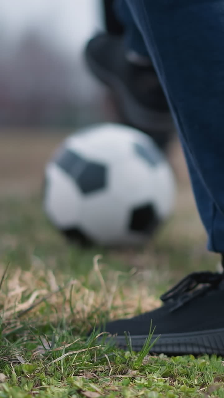 Blurred close-up of someone passing a football to another person who traps it under their right foot, the background features a grassy field with a blurred view of people