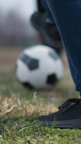 blurred close-up of someone passing a football to another person who traps it under their right foot, the background features a grassy field with a blurred view of people