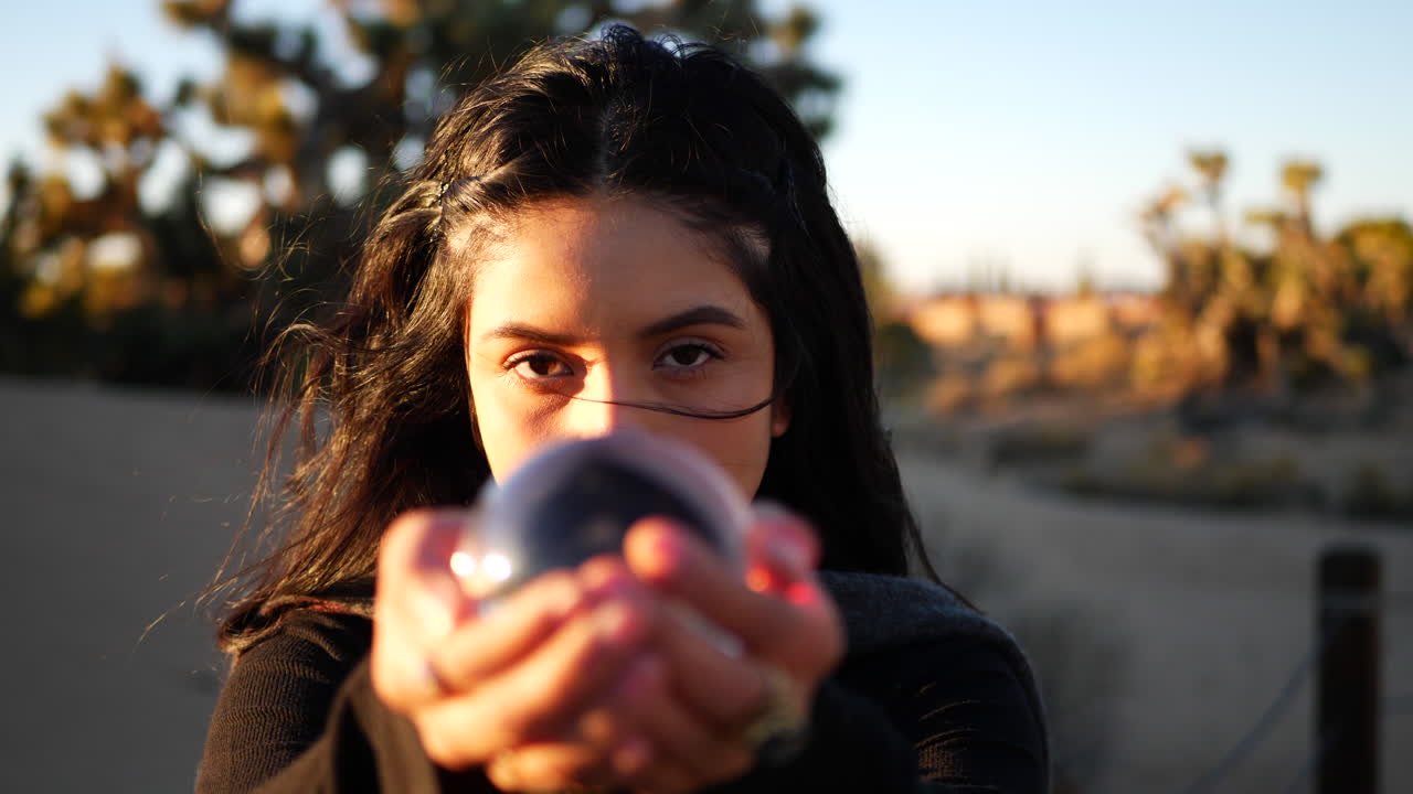 Looking into the eyes of a mysterious beautiful girl wizard holding her magic crystal ball out while casting an enchanting spell