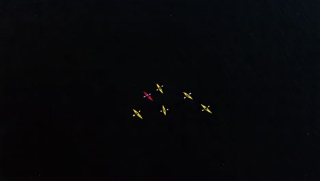 aerial view of kayakers in formation on dark waters, showcasing the colorful canoes and the serenity of nature during a calm day