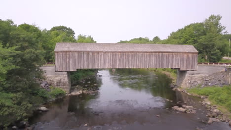 Aerial-shot-flying-over-the-Piscataquls-River-and-the-roof-of-the-lowes-covered-wooden-bridge-in-Maine