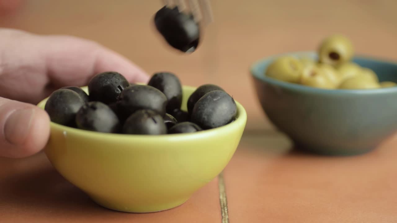 Hand snacking on black olives with fork close up shot