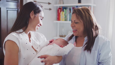 young hispanic mother holding her baby son with grandmother looking on, waist up, close up