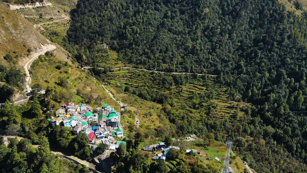 una toma aérea de un avión no tripulado que destaca un hermoso pueblo situado en las laderas de altas montañas verdes.