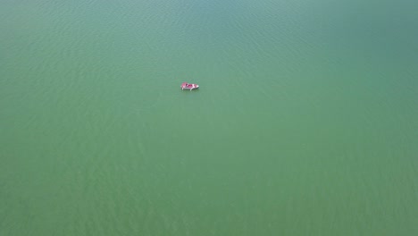 Toma-Aérea-De-Aproximación-Al-Lago-Con-Un-Barco-Flotando-En-El-Medio,-Toma-De-Arriba-Hacia-Abajo