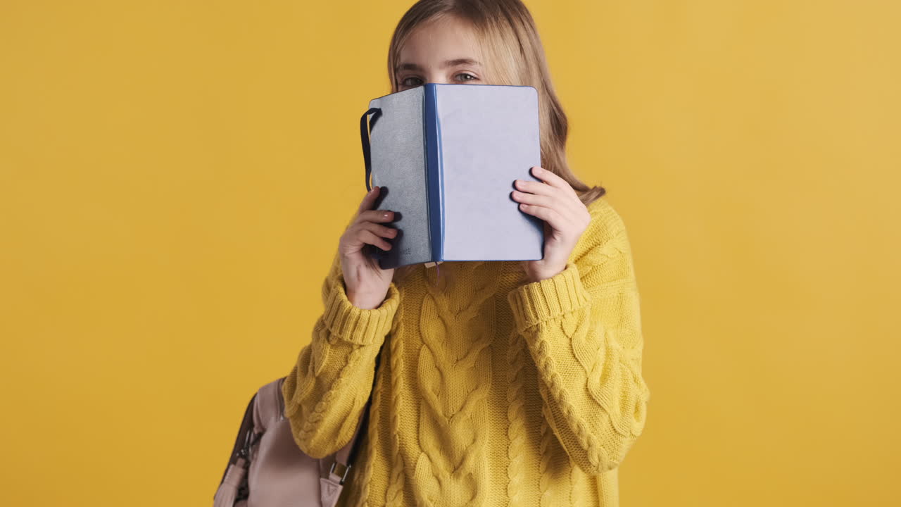 Happy teenage Caucasian girl student holding notebook in front of her head.