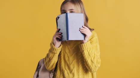 happy teenage caucasian girl student holding notebook in front of her head.