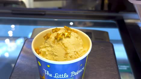 a hand adds crunchy toppings to ice cream in a bangkok shop. bright lighting highlights the detailed process