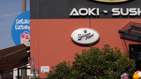 exterior view of a sushi restaurant in germany, featuring the aoki-sushi logo on the wall. the scene captures a blend of japanese cuisine and modern architecture, set in a european urban environment.