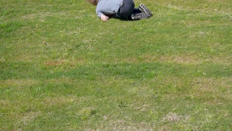 Lächelnder,-Glücklicher-Junge,-Der-An-Einem-Sonnigen-Tag-Lachend-Den-Grasbewachsenen-Hügel-Hinunterrollt