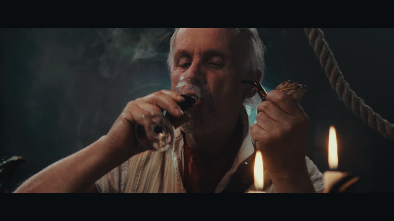 An old pirate eats and drinks inside the sailing ship cabin
