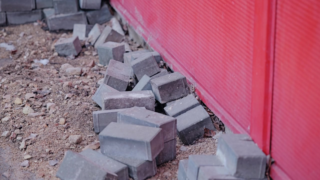 Stacked paving bricks lie beside prepared ground, upcoming sidewalk construction