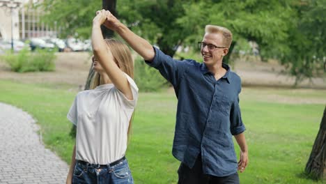 una joven pareja positiva camina tomados de la mano, se reúnen en un parque de la ciudad de verano. la niña y el niño son rubios. caminata feliz en el parque. vista posterior