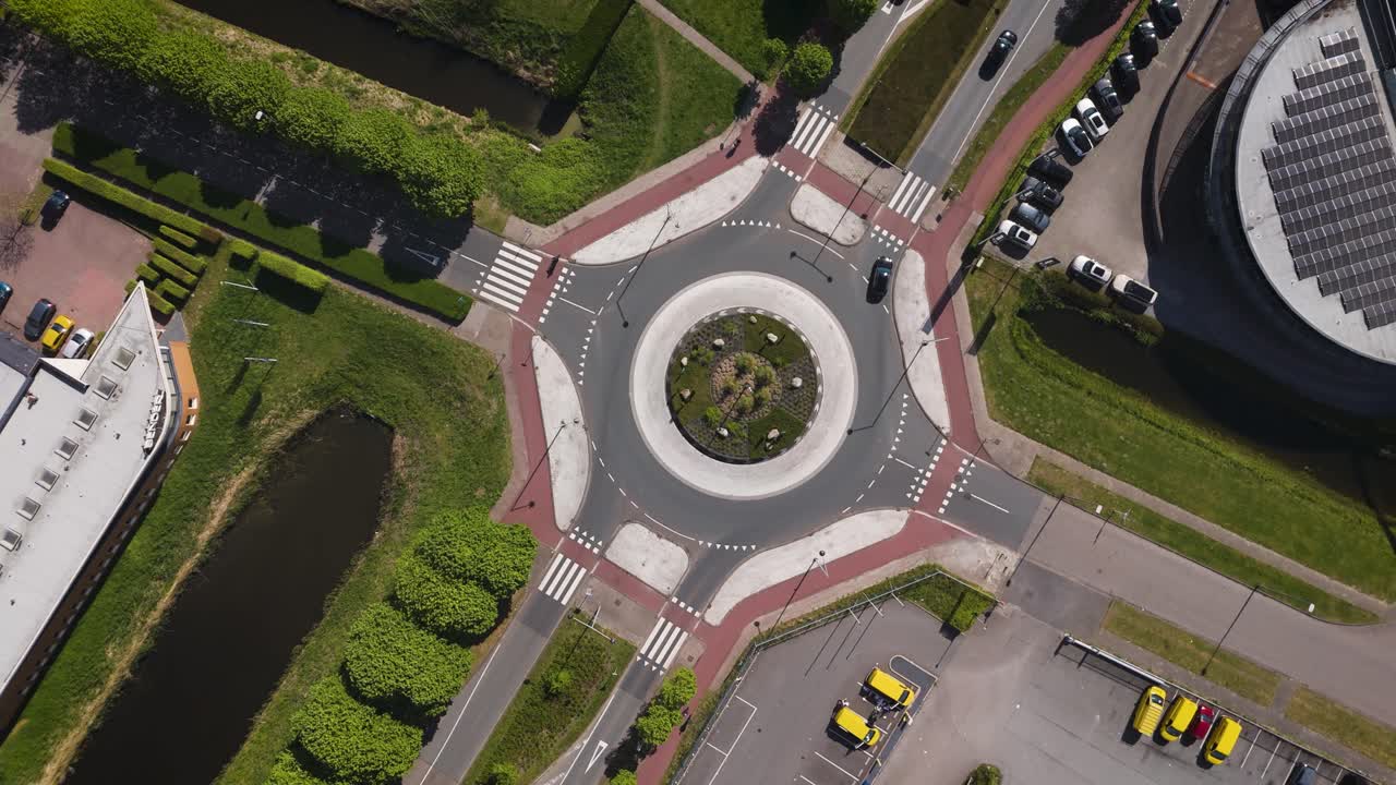 Crisp overhead drone view of a modern Dutch roundabout showcasing organized traffic flow, bike lanes, and green surroundings, ideal for urban planning themes.