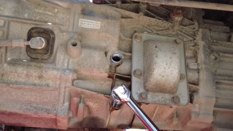 a male using a socket wrench to tight up a bolt under a car, static close up