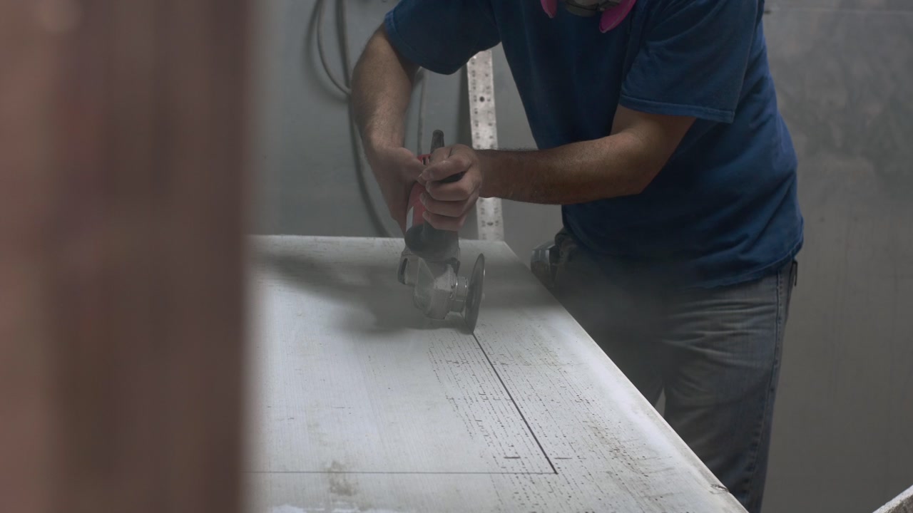 Worker using handheld router to cut straight groove into large white refractory board.