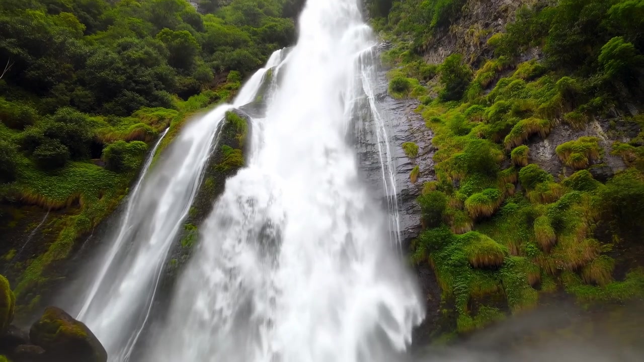 Potente cascata che scende attraverso una foresta lussureggiante, prospettiva cinematografica da drone, acqua bianca che si getta sul muschio.
