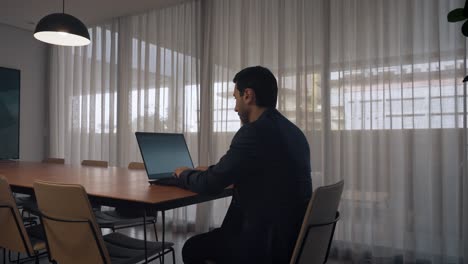 focused executive man typing on his laptop while seated in a modern meeting room, corporate environment.