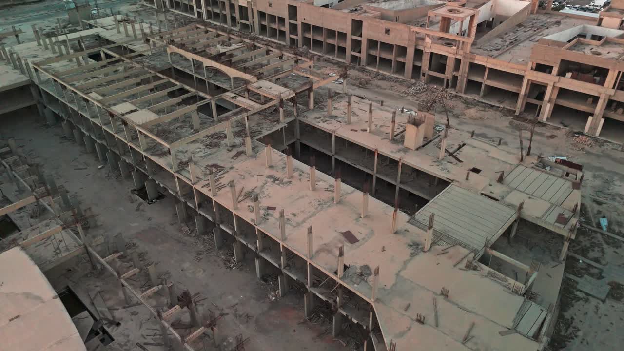 Vista cinematografica con drone di un enorme complesso di cemento incompiuto con barre d'armatura a vista, cortili vuoti, piani crollati e detriti: un megaprogetto abbandonato, ideale per aree urbane degradate, sicurezza e settore immobiliare