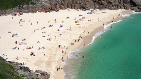 aerial view of porthcurno beach in cornwall full of tourists, swimmers, surfers and families having fun on a beautiful spring sunny day