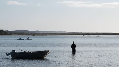 sihouette de pescador zancudo con bote amarrado y kayakistas