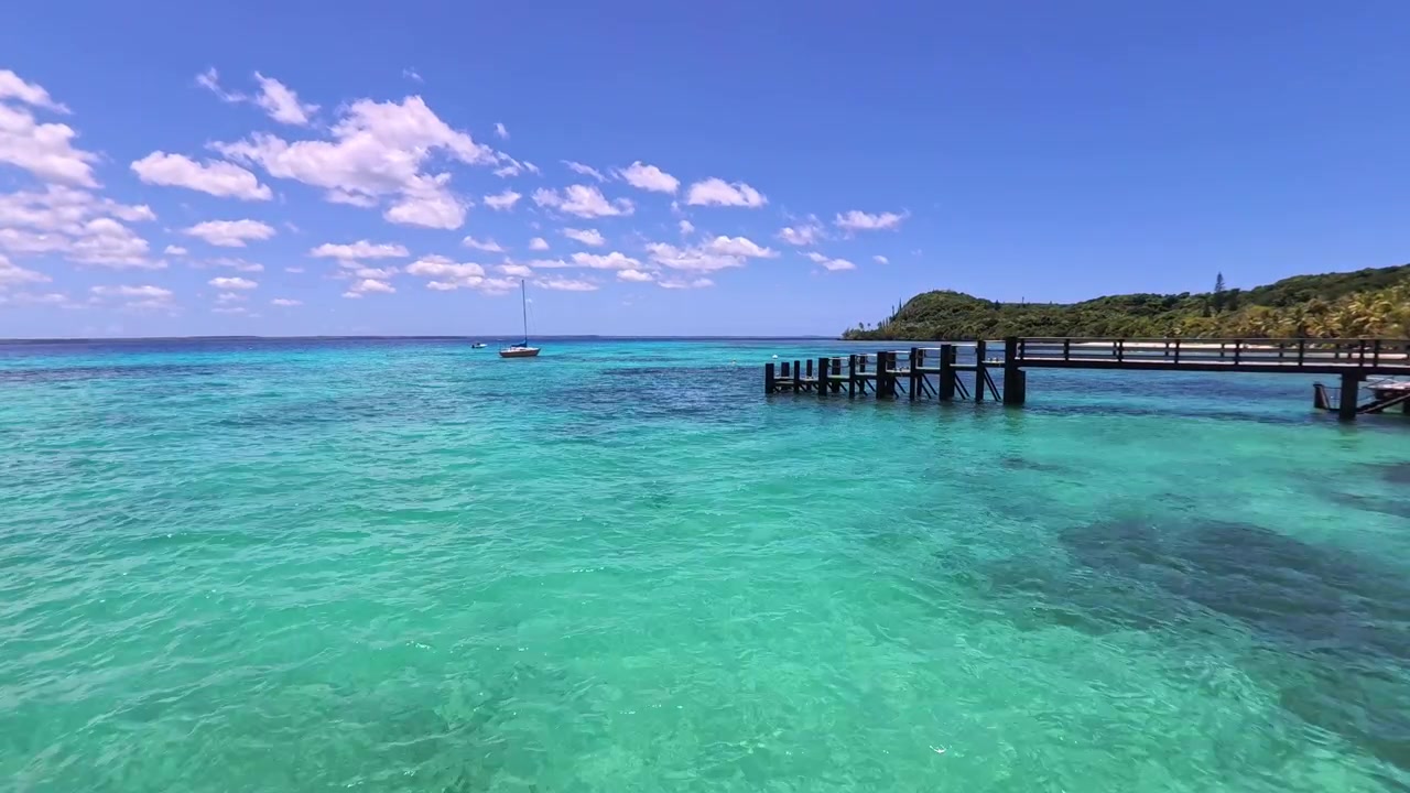 Acqua calma turchese dell'oceano con un molo e una barca a vela vicino a un'isola tropicale