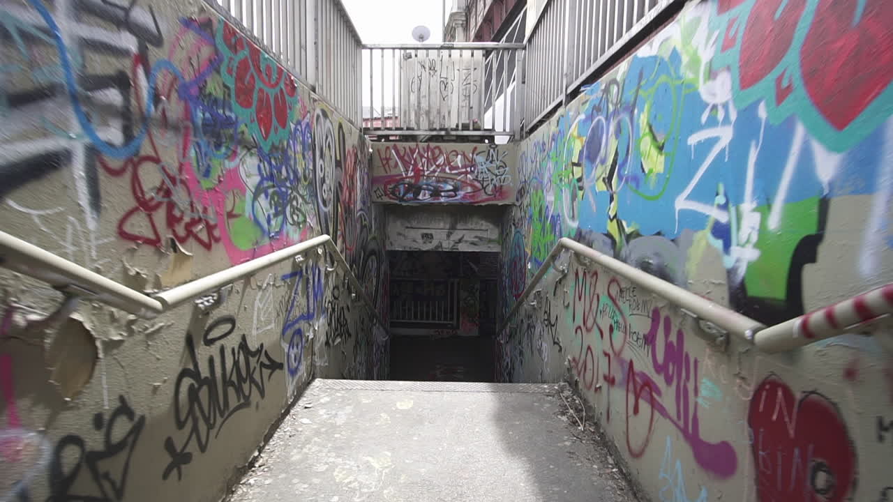 Carrellata in avanti attraverso scale che conducono a un tunnel con graffiti sui muri