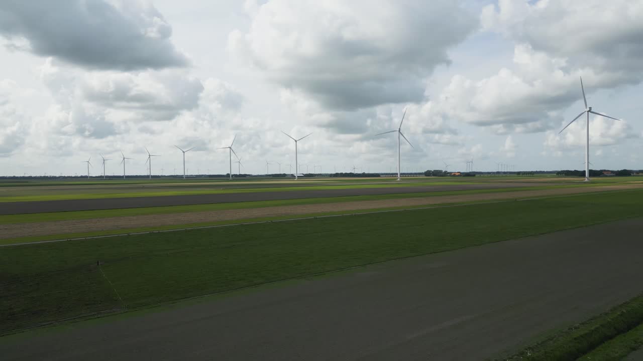 Aerial footage of tall wind turbines on open farmland in the Netherlands with clouds in the background