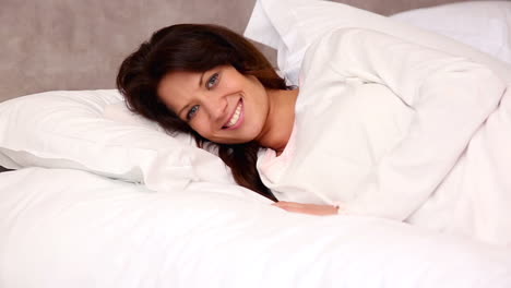 Pretty-brunette-lying-in-bed-smiling-at-camera