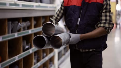 Unrecognizable-worker-walks-with-water-pipes-in-plumbing-or-hardware-store,-cropped