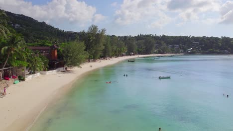 4k aerial drone pull back shot of salad beach on koh phangan in thailand with fishing boats, teal water, coral, and green jungles