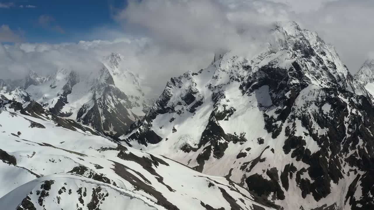 Volo aereo tra le nuvole di montagna sopra splendide vette innevate e ghiacciai.