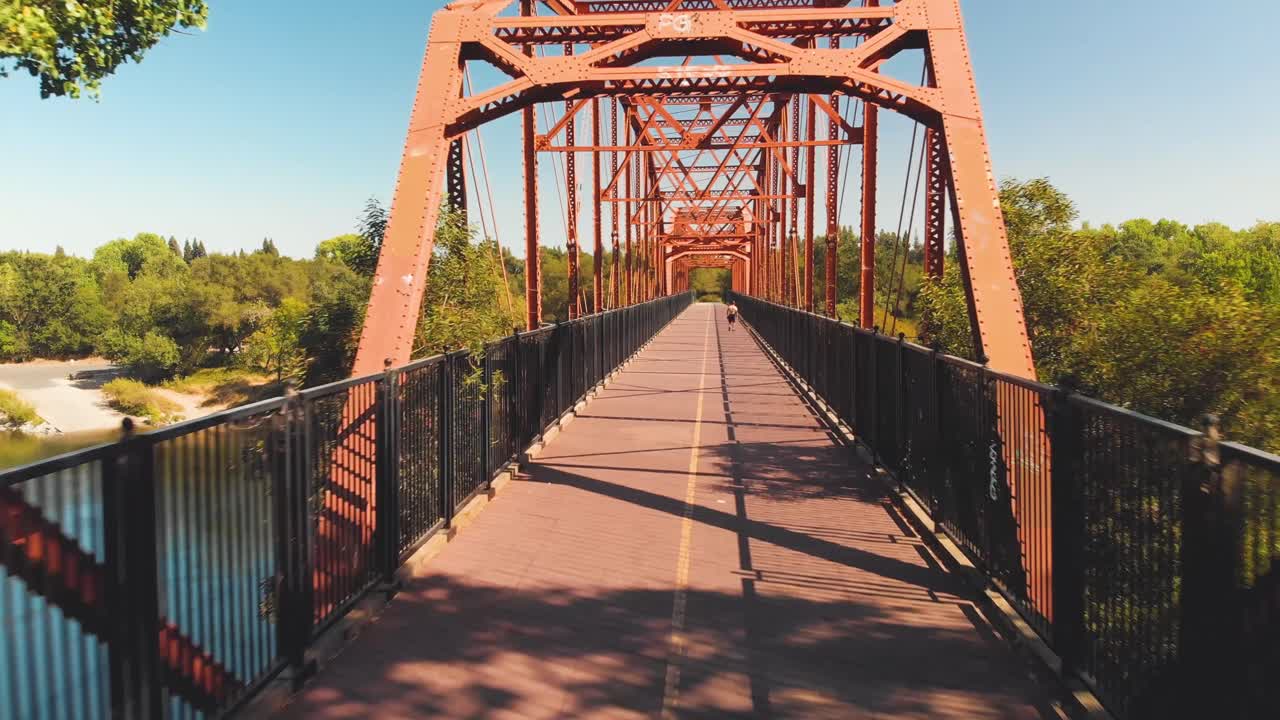 hombre paseando un perro en el puente fair oaks sobre el río americano en california - vista aérea de drones volando a través del puente