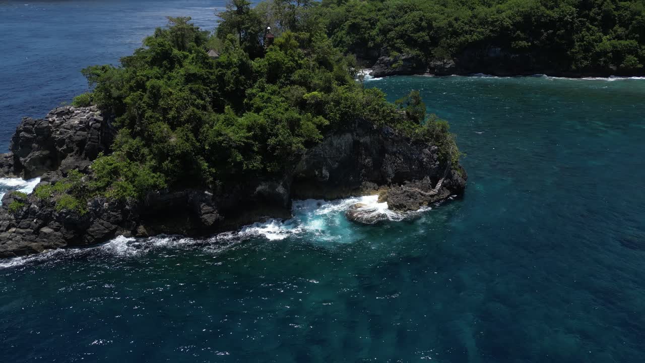 A tiny island surrounded by blue water off the coast of Nusa Penida island in Indonesia