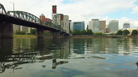 4k nice low on the water shot with slight pan left to right of hawthorne bridge crossing willamette river toward downtown portland, oregon skyline with mostly cloudy sky