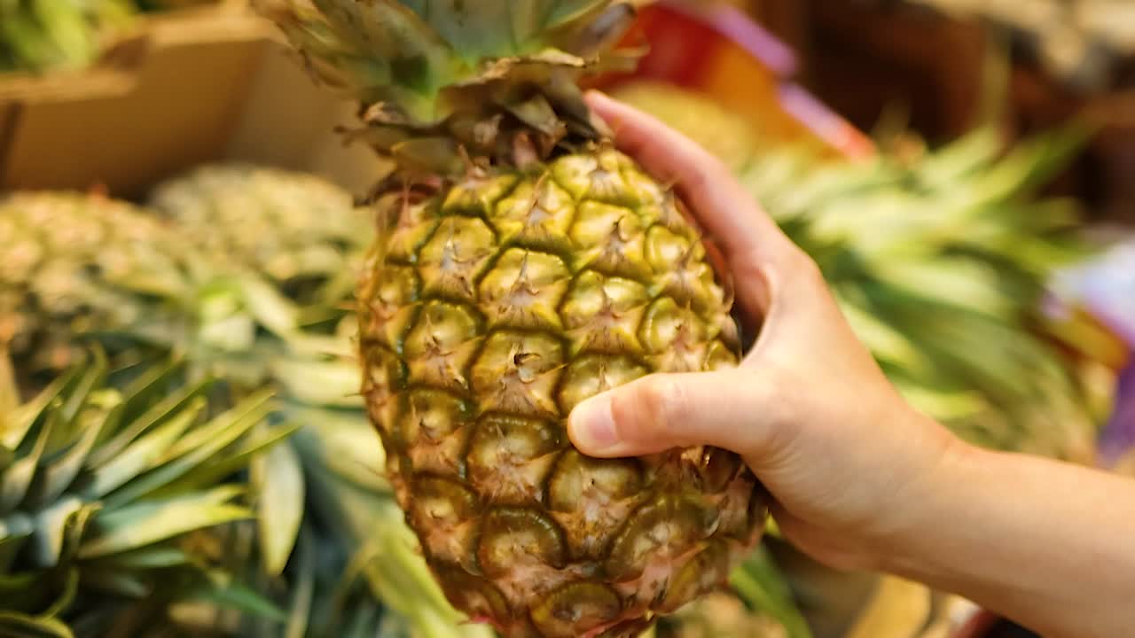 A person's hand picks up and examines a fresh pineapple from a grocery display