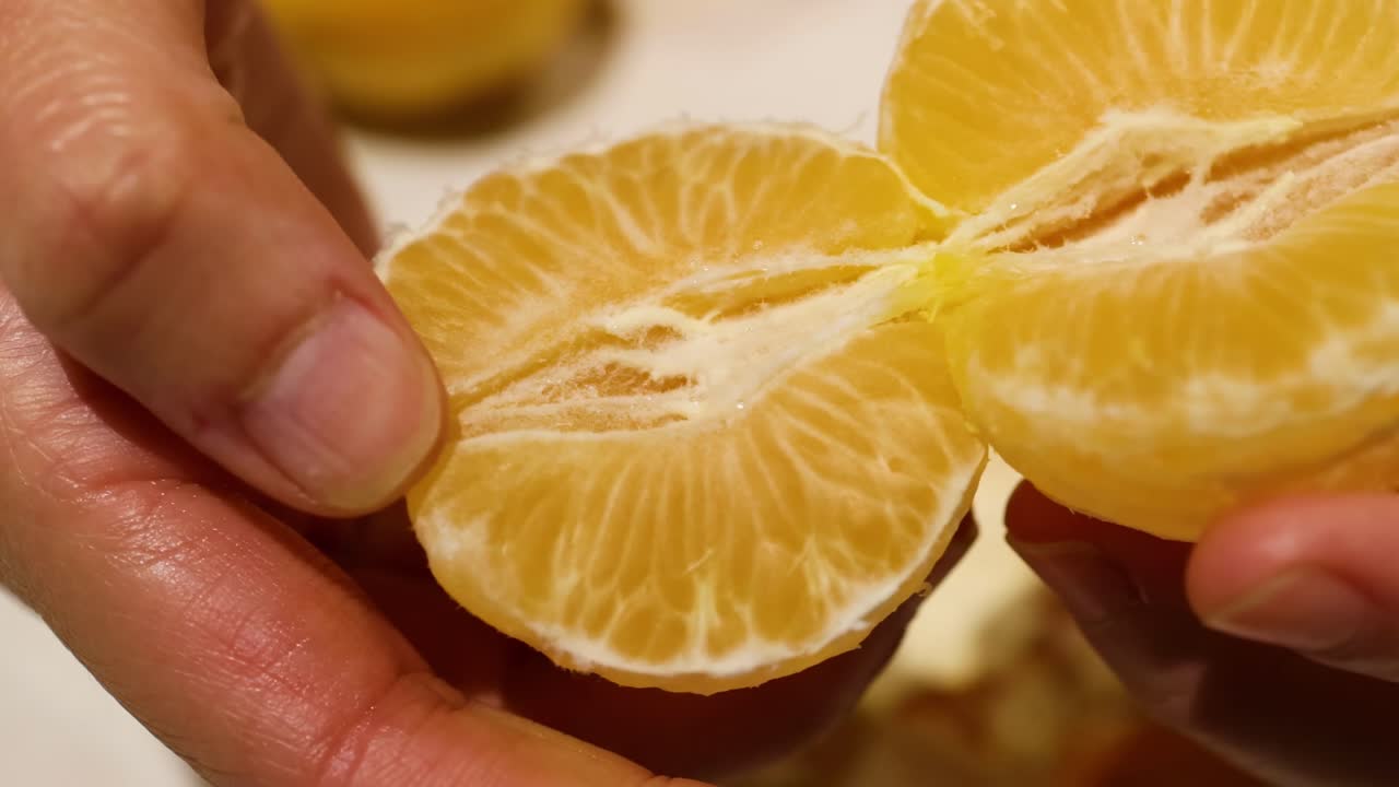 Close-up of hands carefully splitting juicy orange segments, highlighting the texture and freshness of the fruit.