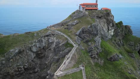 El-Retroceso-Del-Dron-Revela-El-Monasterio-En-La-Isla-De-Gaztelugatxe,-Acantilados-Verdes-Y-Olas-Tranquilas-Del-Océano,-España-Vasca