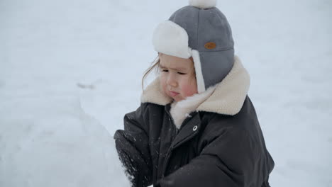 baby girl playing with snow and squeezing by hand then goes to her eyes