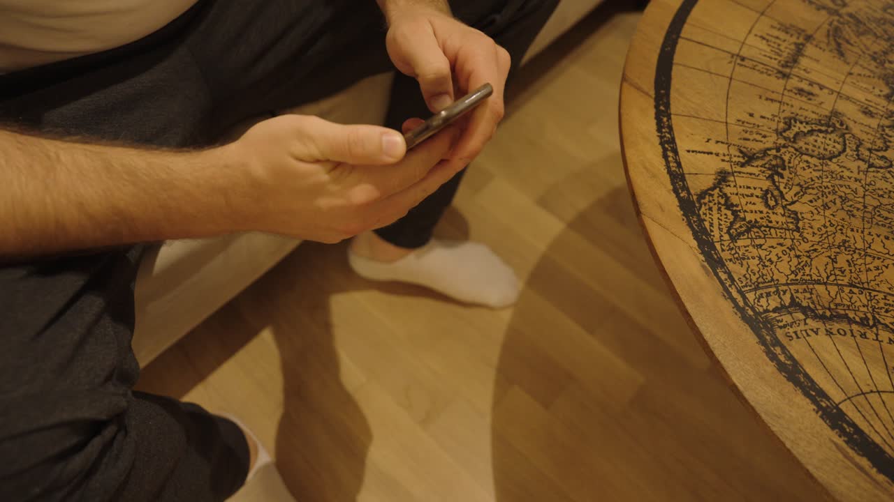 Uno smartphone scivola dalle mani di un uomo e cade sul pavimento al rallentatore. Il dispositivo rimane funzionante, mostrando un realistico incidente domestico quotidiano.