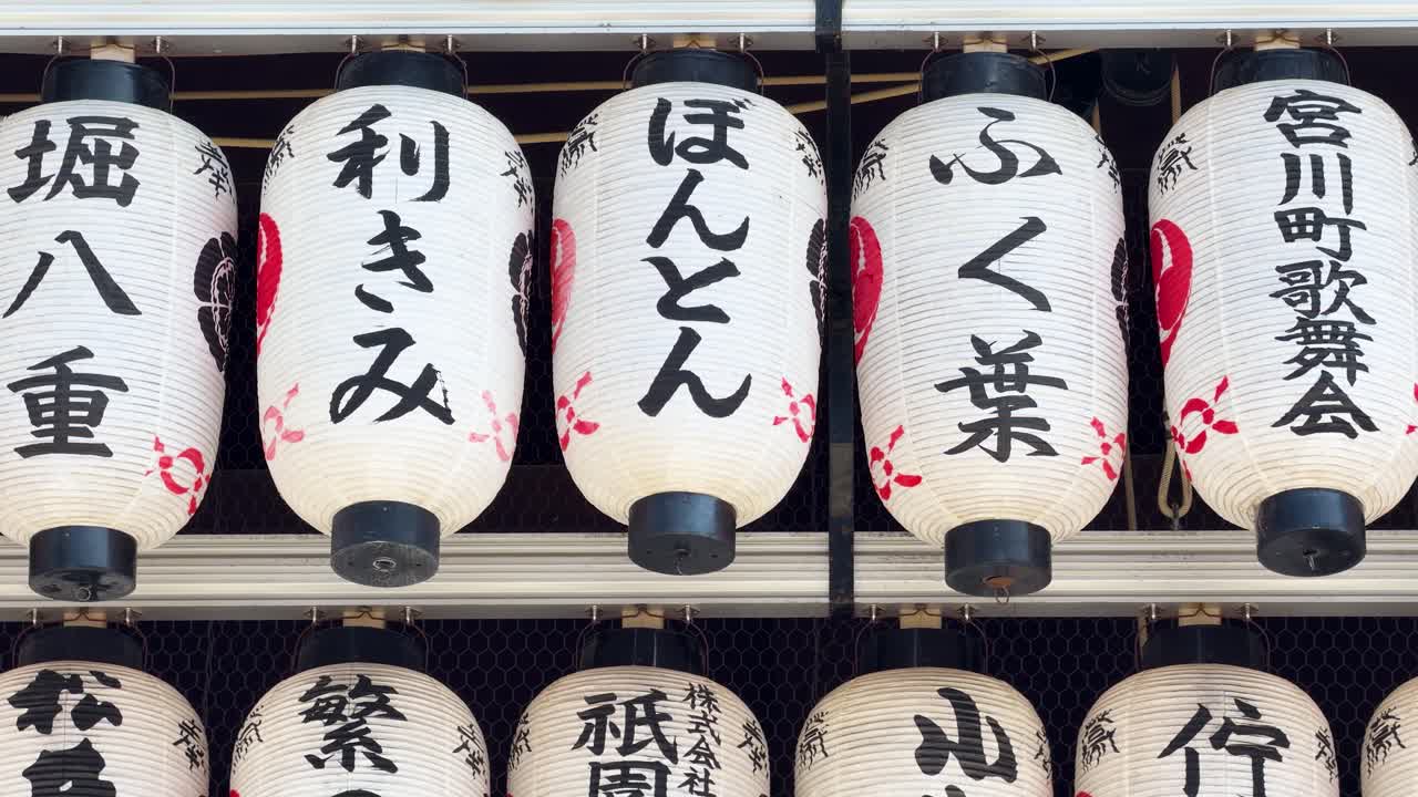 File di lanterne di carta bianche con calligrafia nera pendono in un santuario tradizionale di Kyoto.