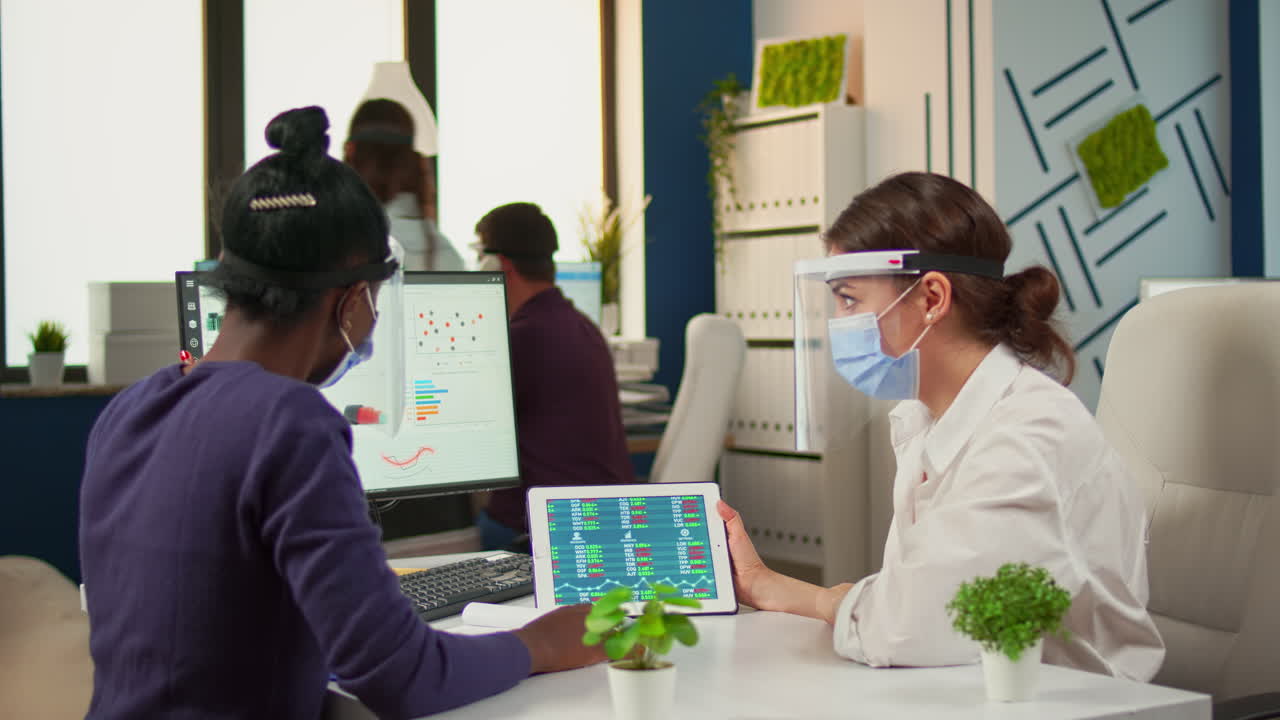 mujeres multiétnicas con máscaras de protección analizando informes anuales